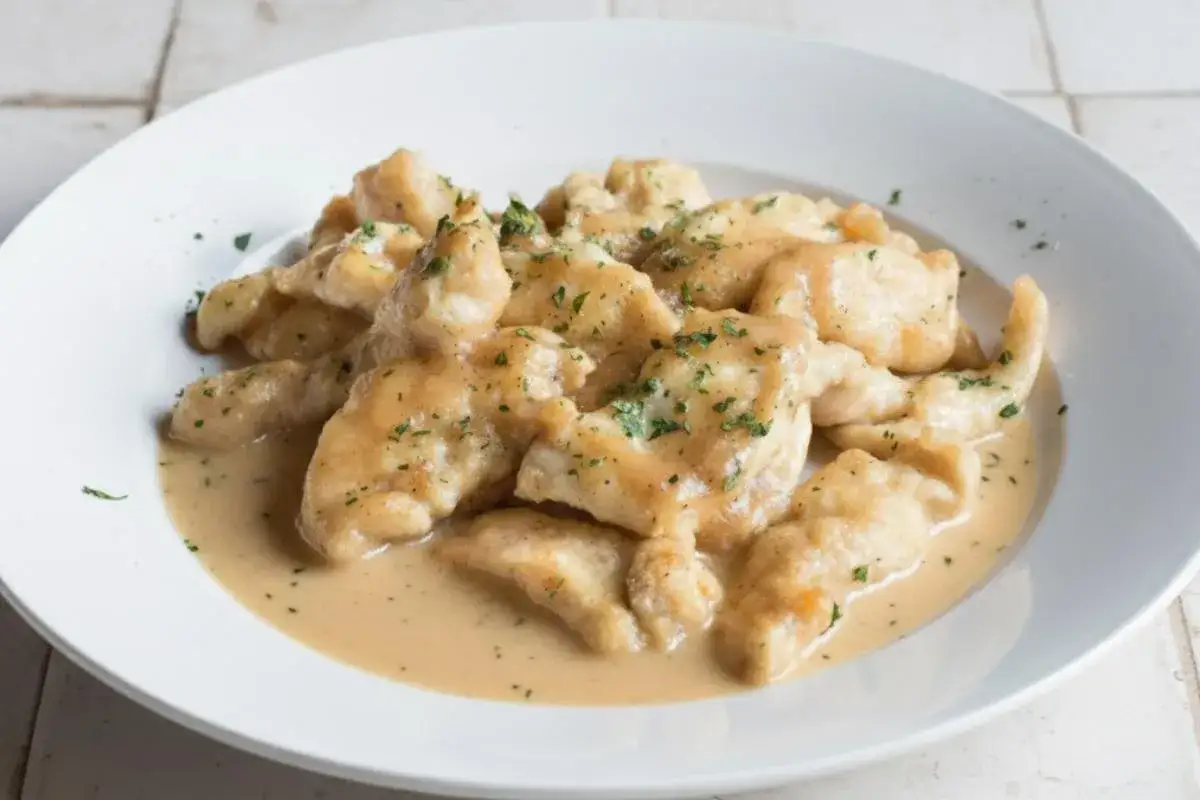 Straccetti di pollo cremosi, un piatto invitante con bocconcini di pollo in una salsa vellutata, guarniti con prezzemolo tritato.