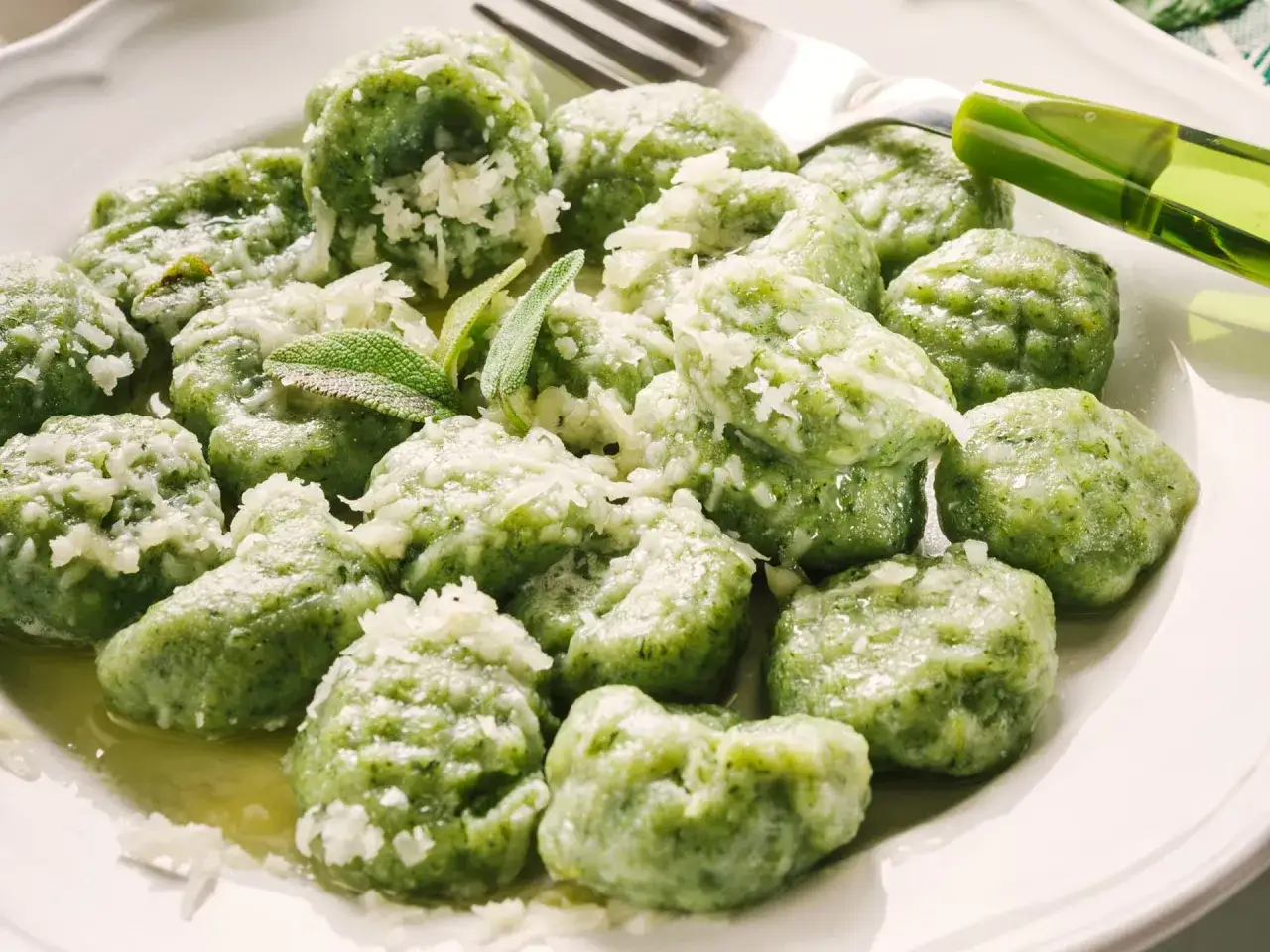 Gnocchi di spinaci freschi, conditi con parmigiano grattugiato e un filo d'olio, pronti per essere gustati.