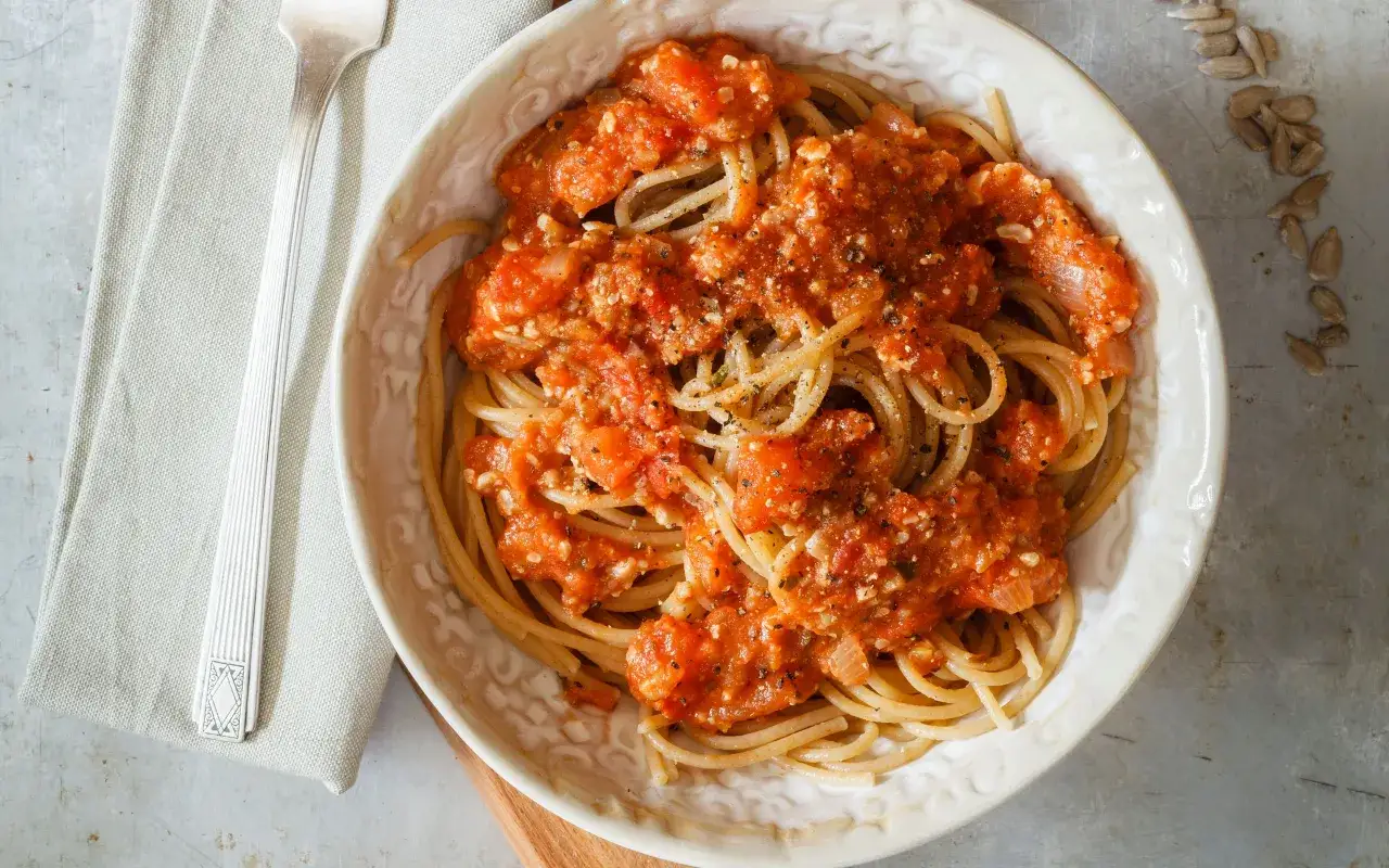 Spaghetti conditi con un saporito rag&ugrave; di verdure, serviti in una ciotola bianca con forchetta e tovagliolo a lato.