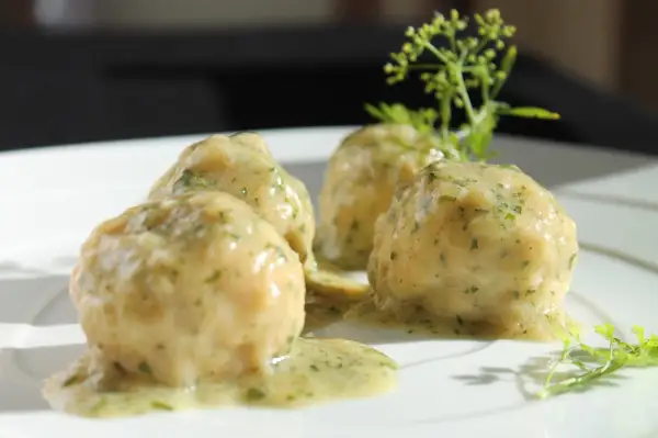 Quattro polpette in bianco su un piatto bianco, condite con una salsa cremosa e erbe aromatiche.