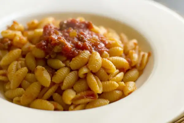 Malloreddus alla campidanese, pasta sarda con sugo di pomodoro e salsiccia, serviti in un piatto bianco.