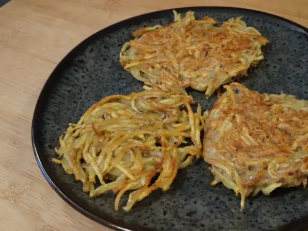 Tre croccanti rosti di patate in padella, dorati e pronti per essere gustati.
