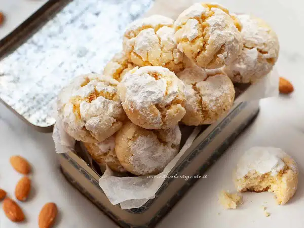 Biscotti con farina di mandorle, spolverati di zucchero a velo, in una scatola vintage. Alcune mandorle intere sono sparse intorno.