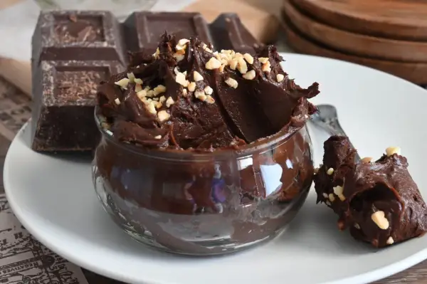Un delizioso budino al cioccolato, cremoso e guarnito con nocciole tritate, accanto a una tavoletta di cioccolato fondente.