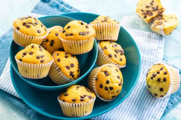 Muffin con gocce di cioccolato dorati e soffici, serviti in una ciotola blu.