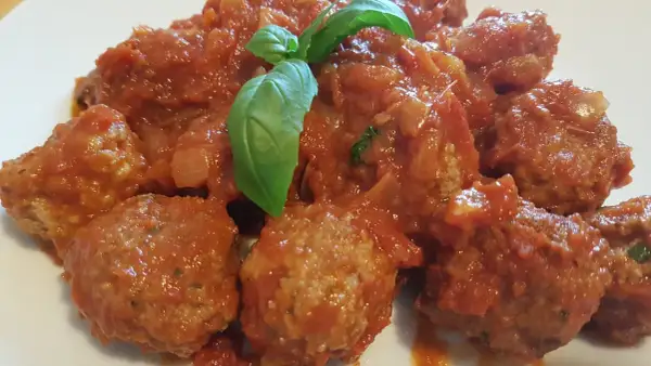Un piatto invitante di polpette di carne morbide immerse in un sugo rosso ricco, guarnite con una foglia di basilico fresco.