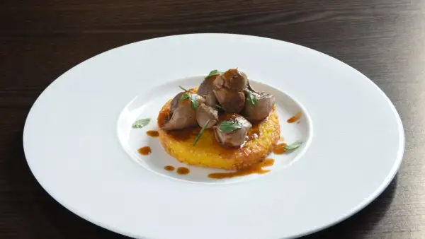 Delizioso riso al salto con bocconcini di carne e salsa bruna, guarnito con erbe fresche su un piatto bianco.