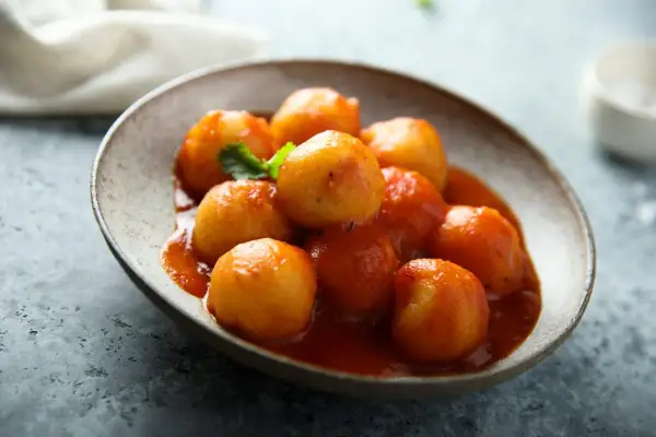 Gnocchi di pane in salsa rossa, un piatto rustico e saporito, servito in una ciotola di ceramica grezza.