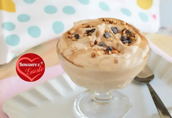 Deliziosa mousse al caffè, guarnita con nocciole tostate e gocce di cioccolato, servita in una coppa di vetro.