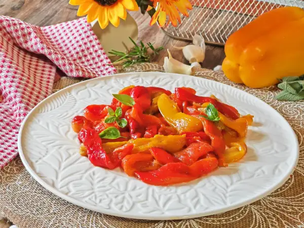 Peperoni rossi e gialli arrostiti in friggitrice ad aria, guarniti con basilico fresco, su un piatto bianco decorato.