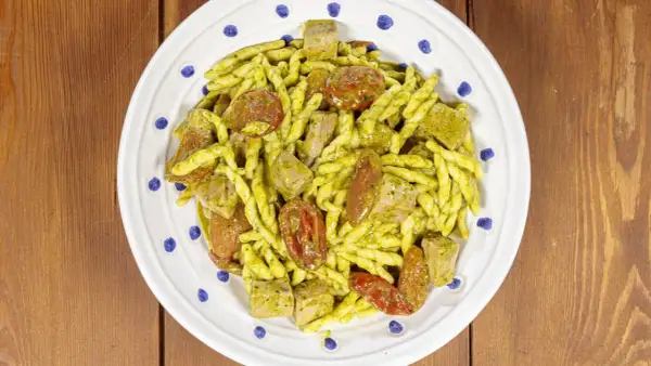 Piatto di trofie alla carlofortina con tonno, pomodorini secchi e pesto, servito su un piatto bianco con decorazioni blu.