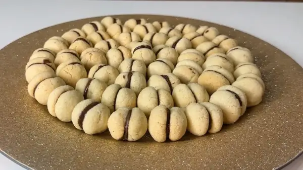 Baci di dama ricetta: biscotti friabili con ripieno di cioccolato, disposti a cerchio su un piatto dorato.
