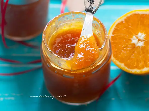 Un vasetto di marmellata di arance fatto in casa, con una fetta d'arancia accanto. La marmellata è lucida e invitante, pronta per essere gustata.