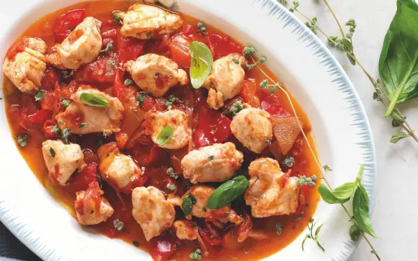 Piatto di coniglio alla cacciatora con pezzi di carne tenera in salsa di pomodoro e peperoni, guarnito con basilico fresco e erbe aromatiche.