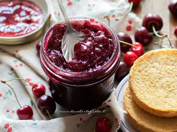 Un barattolo pieno di marmellata di ciliegie fatta in casa, con ciliegie fresche e fette biscottate.