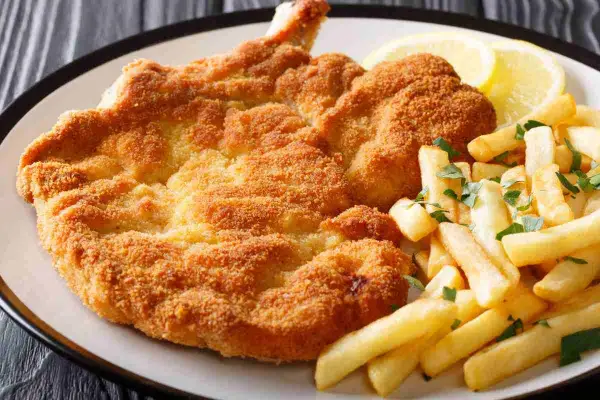 Cotoletta alla milanese dorata e croccante, servita con patatine fritte e spicchi di limone.