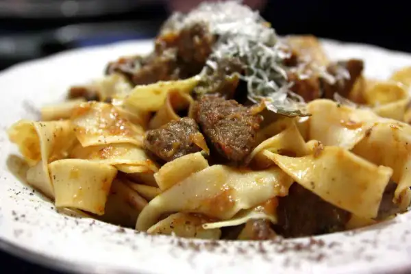 Pappardelle al cinghiale fumanti, con pezzi di carne succulenta e una spolverata di parmigiano.