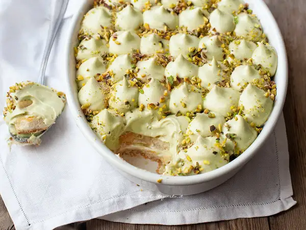 Delizioso tiramisù senza caffè, con crema al pistacchio e biscotti savoiardi, guarnito con granella di pistacchi.