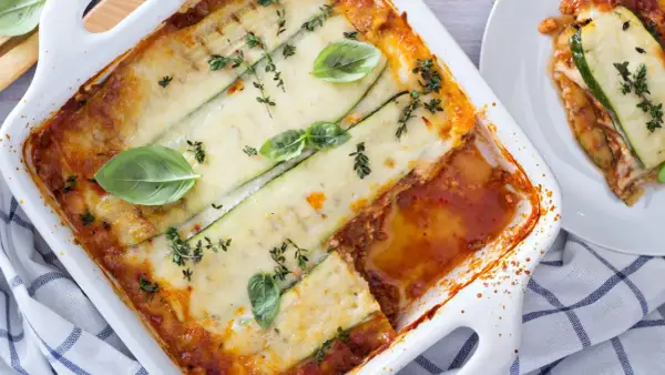 Lasagne di zucchine al forno, dorate e filanti, guarnite con basilico fresco e timo. Un piatto leggero e gustoso.