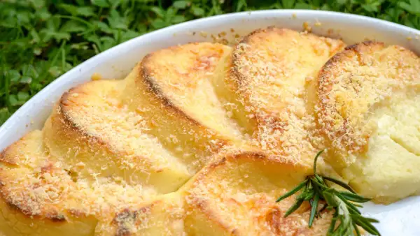 Gnocchi alla romana dorati e gratinati, serviti in una teglia bianca con un rametto di rosmarino.