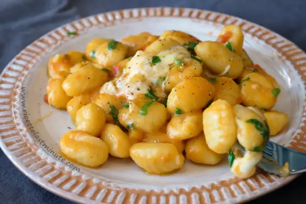 Gnocchi di spinaci cremosi con formaggio filante e prezzemolo fresco, serviti su un piatto decorato.