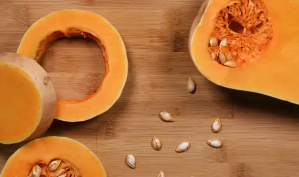 Fette di zucca pronte per essere cotte in padella, con semi sparsi sul tagliere di legno.