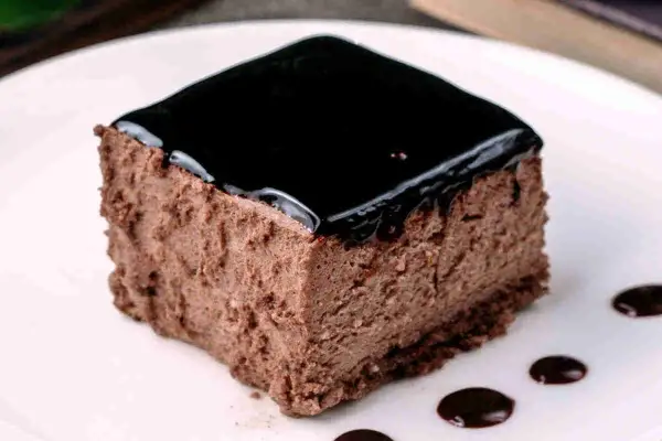 Un delizioso semifreddo al cioccolato, con una lucida glassa scura e gocce di salsa al cioccolato sul piatto bianco.