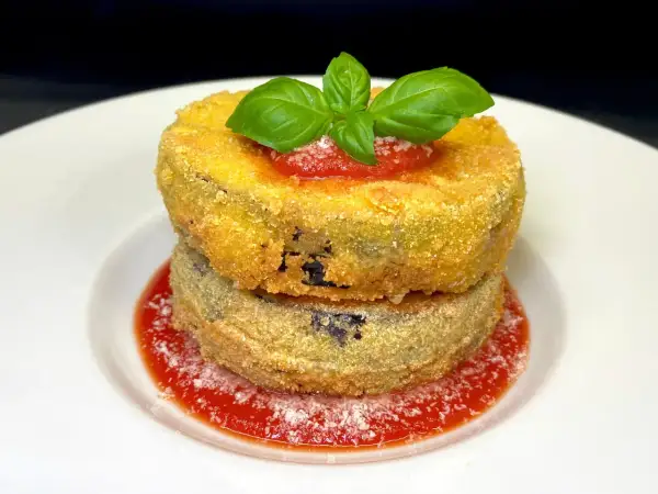 Due cordon bleu di melanzane impilati, dorati e croccanti, su salsa di pomodoro e basilico fresco.