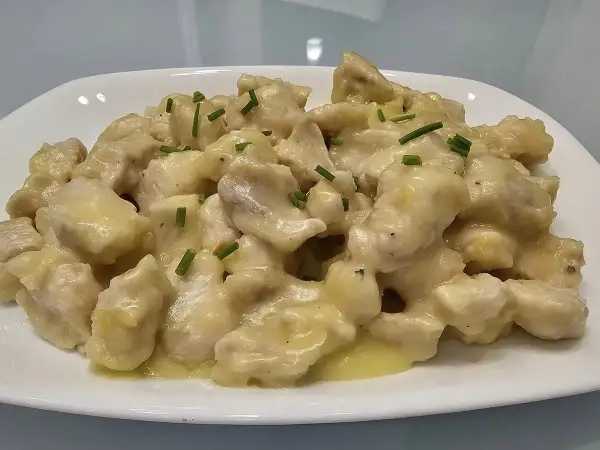 Straccetti di pollo cremosi, un piatto invitante con bocconcini di pollo in una salsa vellutata, guarniti con erba cipollina fresca.