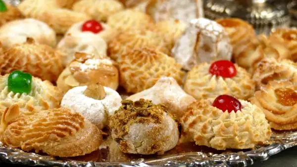 Vassoio pieno di biscotti alle mandorle morbidi, alcuni decorati con ciliegie candite, mandorle e pistacchi.