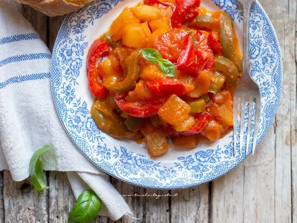 Un piatto di peperonata con patate, colorato e invitante, guarnito con basilico fresco.