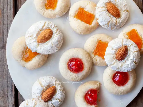 Biscotti alla pasta di mandorle con mandorle intere, marmellata d'arancia e ciliegie candite, spolverati di zucchero a velo.