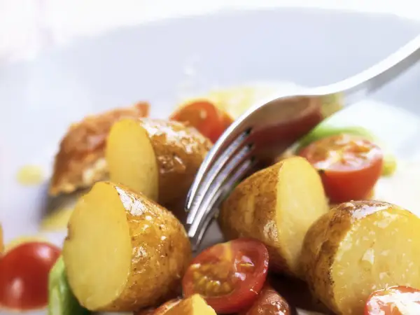Patate novelle tagliate a metà, pomodorini e un tocco di verde compongono questa fresca insalata di patate estiva, pronta per essere gustata.